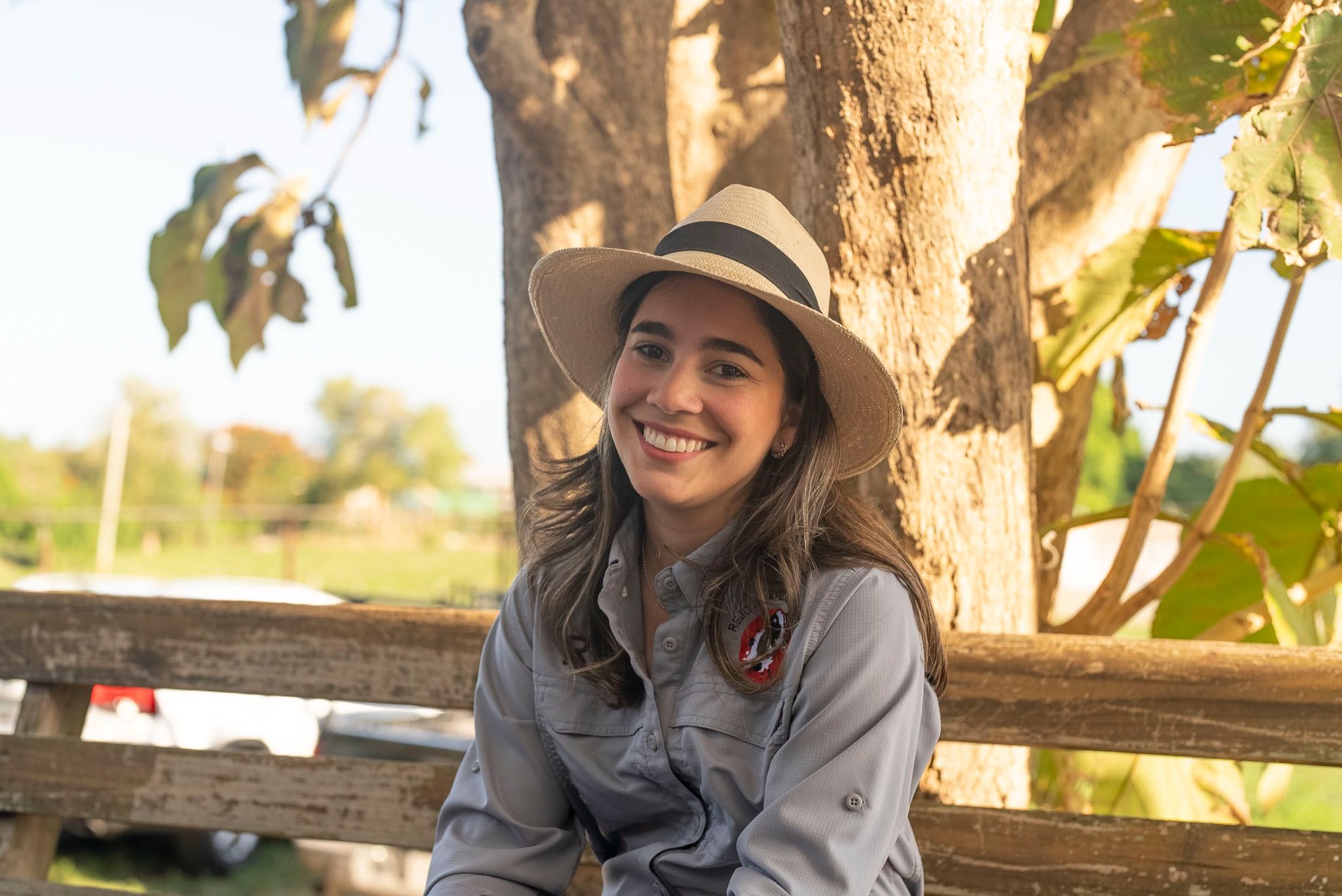 Agricultora con sombrero sonriendo bajo un árbol