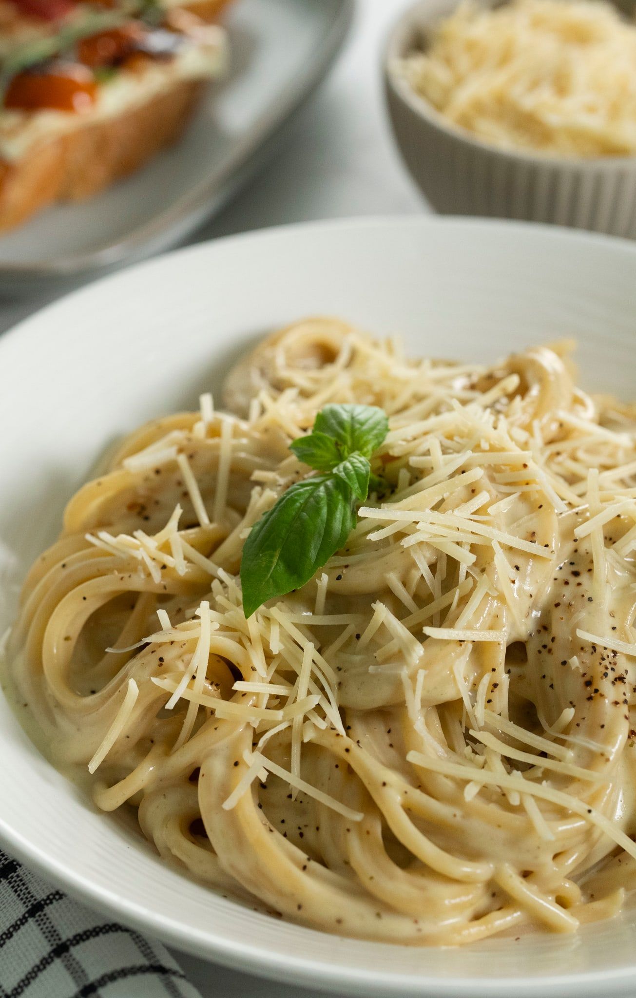 Spaghetti en salsa blanca con queso rallado y albahaca