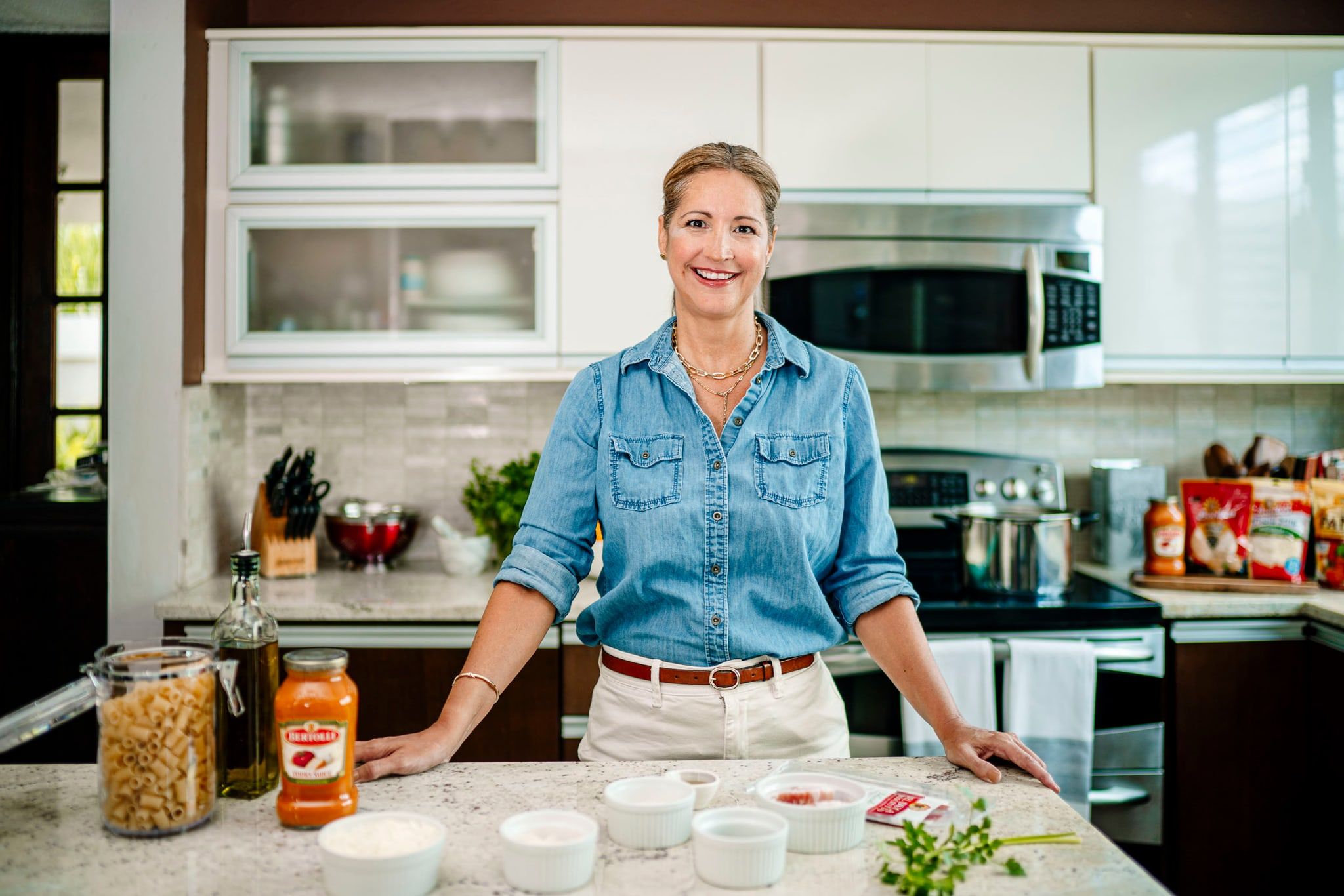 Creadora de contenido sonriendo en su cocina, con pasta y salsa sobre la encimera