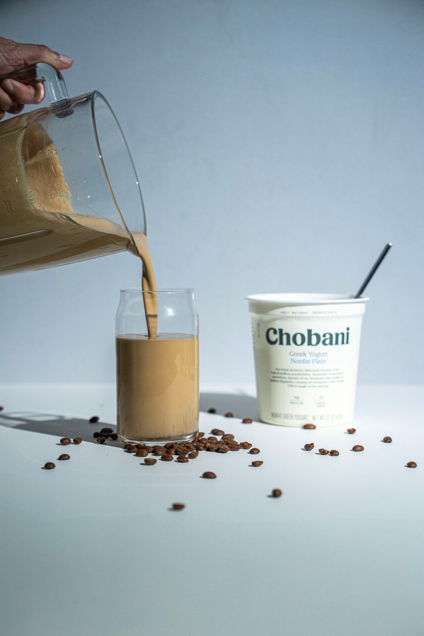 Leche cayendo en un vaso de café frío con granos alrededor